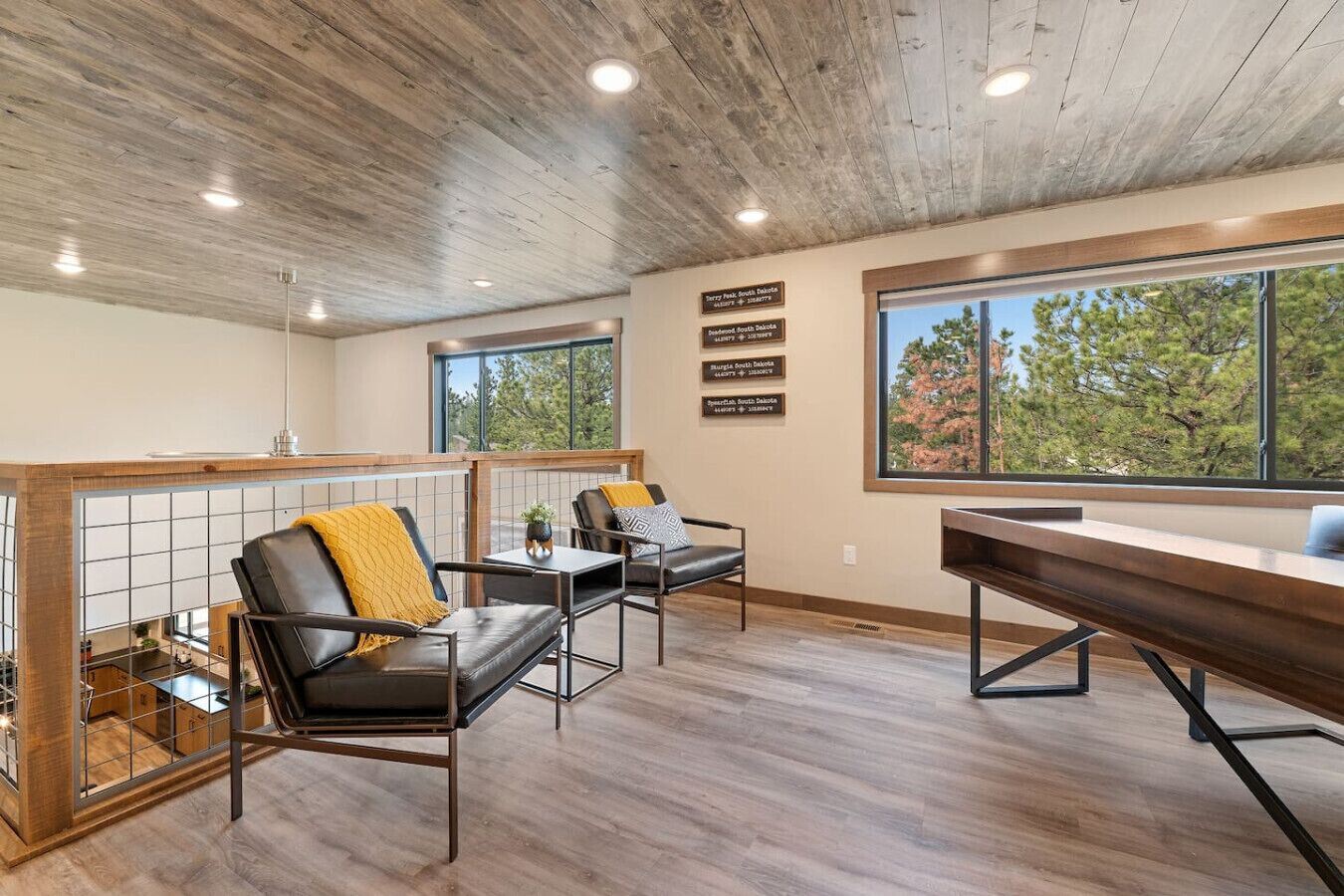 Un interior moderno con techo de madera, un ventanal con vistas a árboles y una zona de estar con dos sillones y una mesa.
