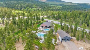 An aerial view of a resort with a swimming pool, a large building with a roof, and a forested landscape in the background. - The Fireside-Hot Tub, Firepit, Fireplace (Lead)