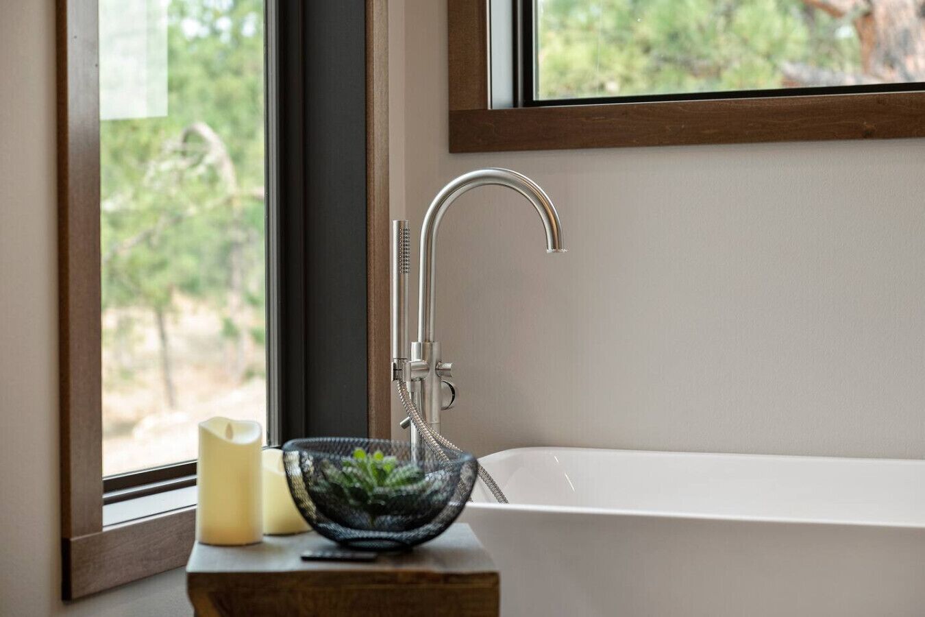 A modern bathroom with a freestanding bathtub, a glass bowl with plants, and a candle on a wooden side table.