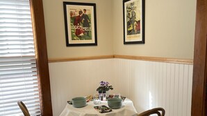 Un comedor con una mesa preparada para dos personas, dos sillas, un florero con flores y dos carteles enmarcados en la pared.