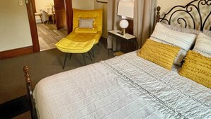 Habitación de hotel con cama, una silla, una mesita de noche, ventilador de techo y ventana con cortinas.