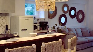 A modern kitchen with a white refrigerator, a coffee machine, and a dining area with wicker chairs and a wooden table. - Design cottage in Drome Provençale (Vinsobres)