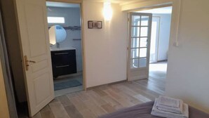 A bedroom with a bed, a bedside table, a door leading to a bathroom, and a view of a hallway.