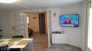 A room with a television mounted on the wall, a dining table with chairs, and a wooden floor.