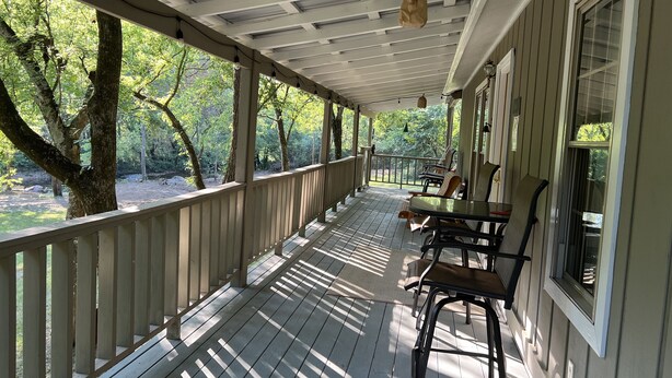 A covered porch with wooden railings, a table, and chairs. - Relax on the Caddo (Caddo Gap)