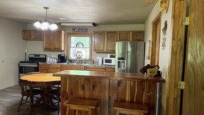 A kitchen with wooden cabinets, a stainless steel refrigerator, a wooden island with stools, and a window with a view of trees. - Relax on the Caddo (Caddo Gap)