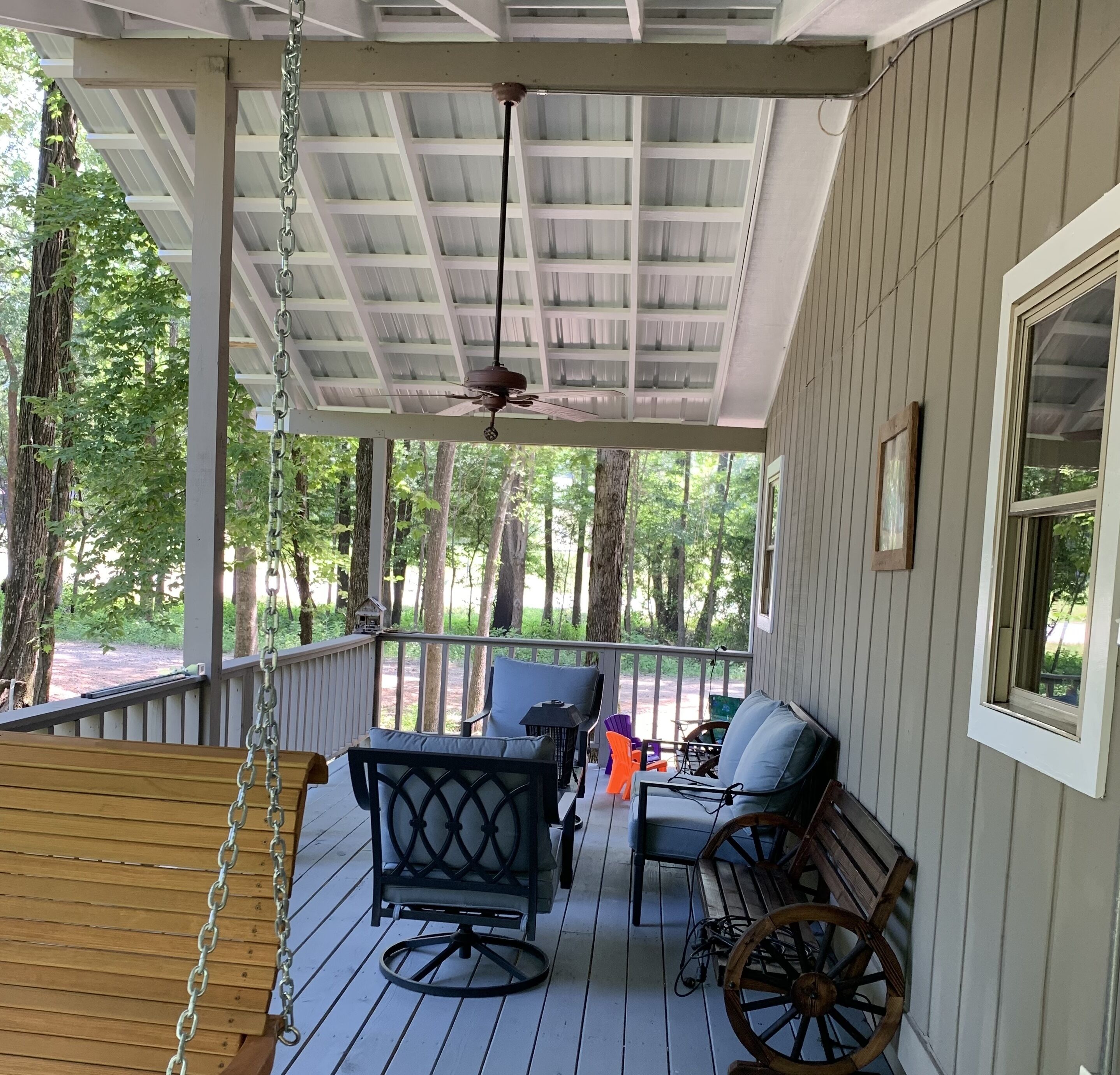 A covered porch with a ceiling fan, wooden swing, and outdoor seating with chairs and a table.