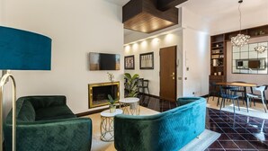 A modern living room with a fireplace, green sofas, a dining area, and a large mirror.