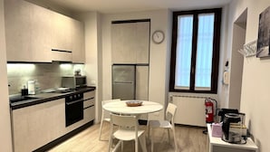 Een kleine keuken met moderne apparatuur, een eethoek met een ronde tafel en stoelen, en een gezellige zithoek met een bank.