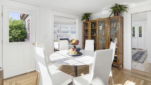Un coin repas avec une table ronde, des chaises blanches et un saladier rempli de fruits. On y trouve également un meuble en bois avec des portes en verre, sur lequel est posée une plante en pot.