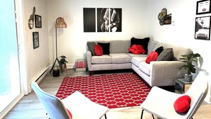 Un soggiorno con un divano grigio, cuscini rossi, un tappeto con motivi rossi e opere d'arte alle pareti.