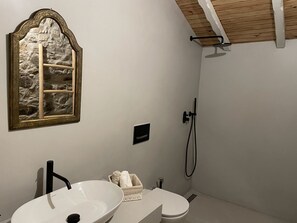 Et badeværelse med hvid vask, toilet, brusebad og en dekorativ stenvæg.