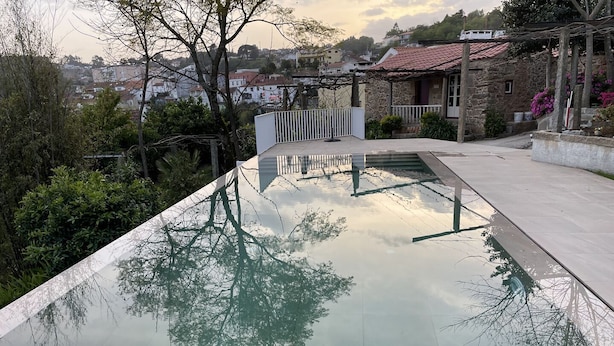 Une piscine à l’eau claire dans laquelle se reflètent les arbres, avec un bâtiment en pierre en arrière-plan.