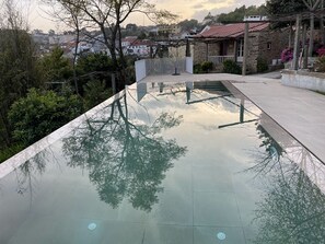 En pool med klart vand, der spejler træer og en stengbygning i baggrunden.