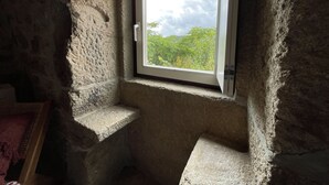 Une pièce aux murs de pierre, avec une petite fenêtre donnant sur un paysage verdoyant.