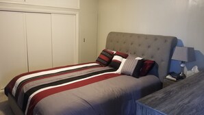 A neatly made bed with striped bedding, a tufted headboard, and a bedside table with a lamp and a tissue box. - Great Bungalow in the gateway to the Black Hills (Sturgis)