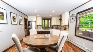 Une cuisine moderne avec une table ronde en bois, des armoires blanches et une grande fenêtre donnant sur un paysage verdoyant.