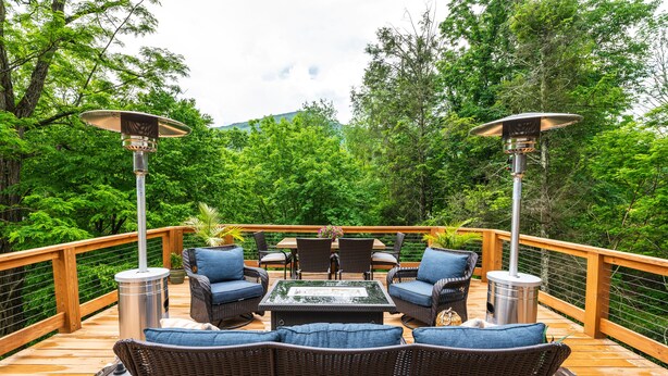 Une terrasse en bois, agrémentée de meubles d’extérieur, notamment des fauteuils en osier et une table, le tout entouré d’une végétation luxuriante.