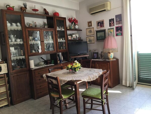 A dining area with a table set for two, surrounded by wooden chairs with green cushions. A television is mounted on the wall above the table. - Pressi Caronte Appartmento in Messina (Messina)
