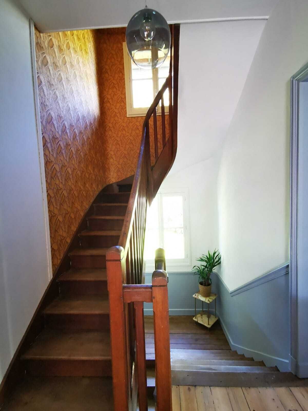 Eine Holztreppe mit Handlauf, die zu einem Zwischenpodest mit Blumentopf und Fenster führt.