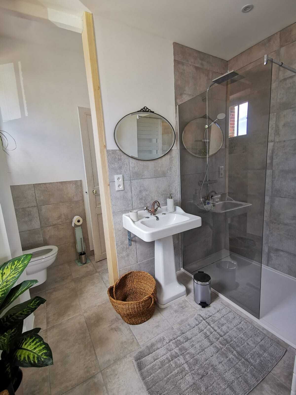 A modern bathroom with a pedestal sink, a glass shower enclosure, and a large mirror.