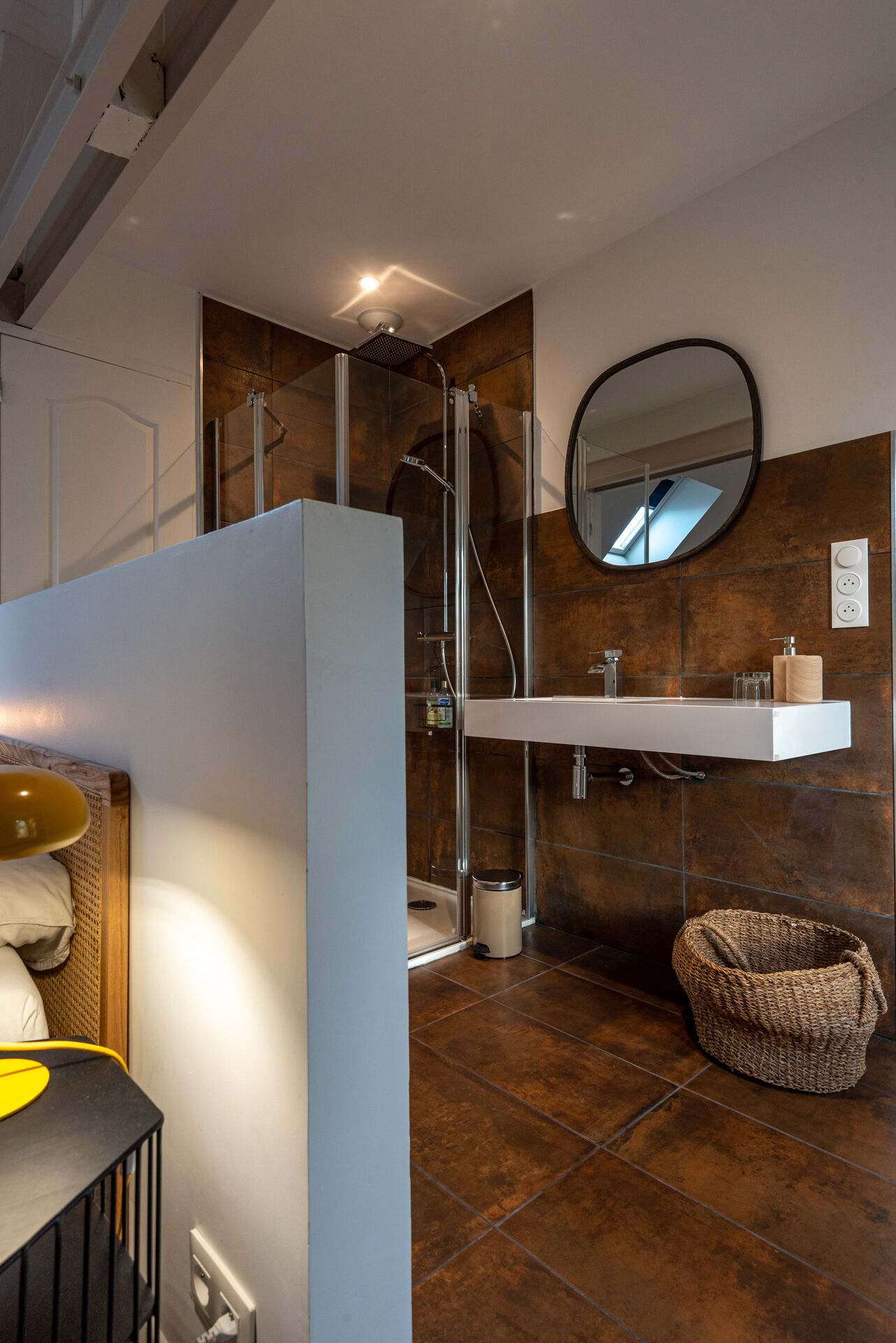 A modern bathroom with a glass shower enclosure, a white sink with a mirror above it, and a woven basket on the floor.
