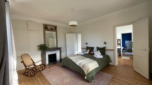 A bedroom with a bed, a chair, a fireplace, and a mirror. - La Villégiature (Coutances)
