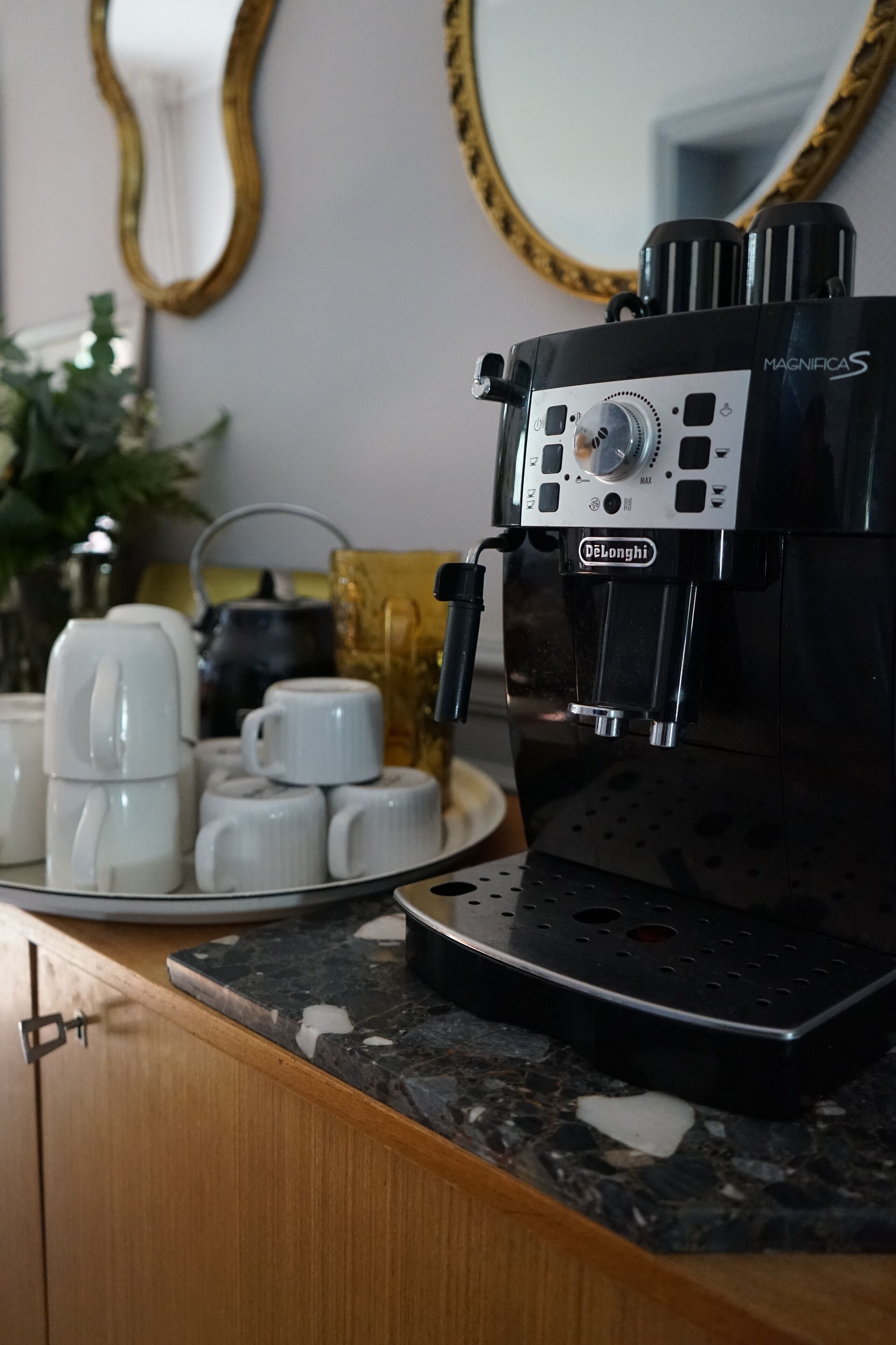 A coffee machine on a countertop with a plate of white cups and a kettle in the background.