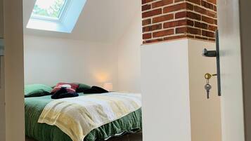 A bedroom with a skylight, a bed with green bedding, a white door with a key, and a brick fireplace.