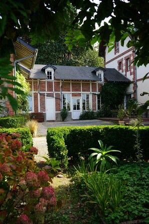 A traditional brick house with a white door, surrounded by well-maintained hedges and a gravel path. - La Villégiature (Coutances)