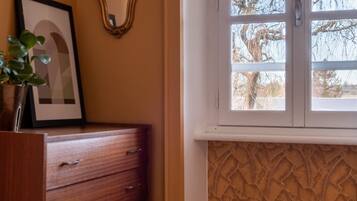 A corner room with a wooden dresser, a framed picture, a mirror, and a window with a view of trees.