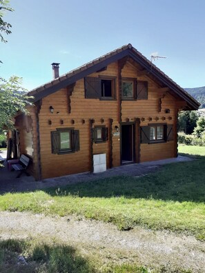 A wooden chalet with two floors, a chimney, and a door with a small porch.