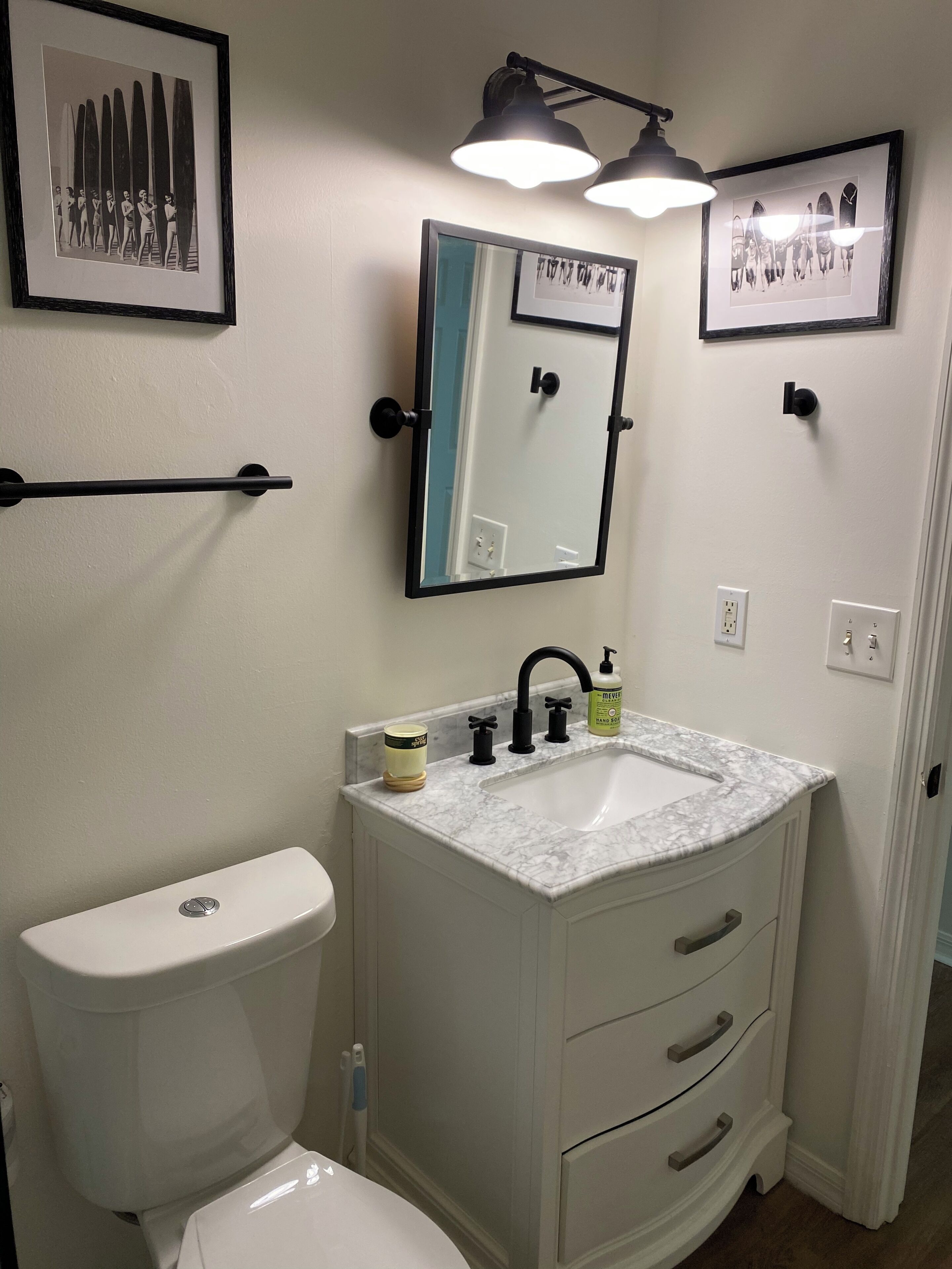 Ein Badezimmer mit Toilette, einem Waschbecken mit Marmorplatte, einem Spiegel und zwei Wandleuchten.