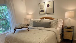 Un lit bien fait, recouvert d’une couvre-lit à rayures, une table de chevet avec une lampe et une fenêtre avec des rideaux.