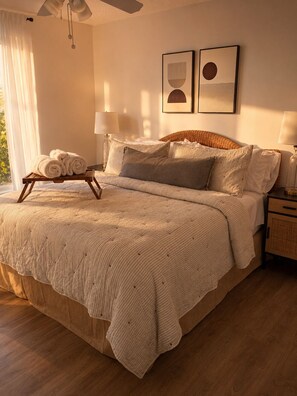 A bedroom with a bed, pillows, a bedside table, a lamp, and a window with curtains.