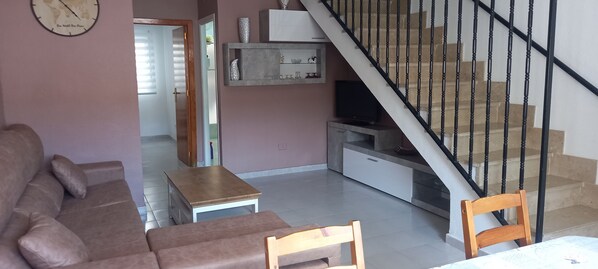 A living room with a sofa, a small table, a TV, and a staircase with a railing.