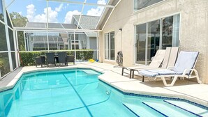 A swimming pool with clear blue water, surrounded by lounge chairs and a covered patio area.