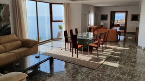 A spacious living area with a glass dining table, comfortable seating, and a large window offering a view of the sea. - Exclusive villa with private pool and gym (Almuñécar)
