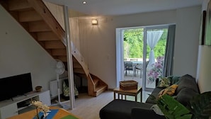 Ein modernes Wohnzimmer mit einer Holztreppe, einem Fernseher, einem Esstisch mit grünen Platzsets und einem schwarzen Sofa.