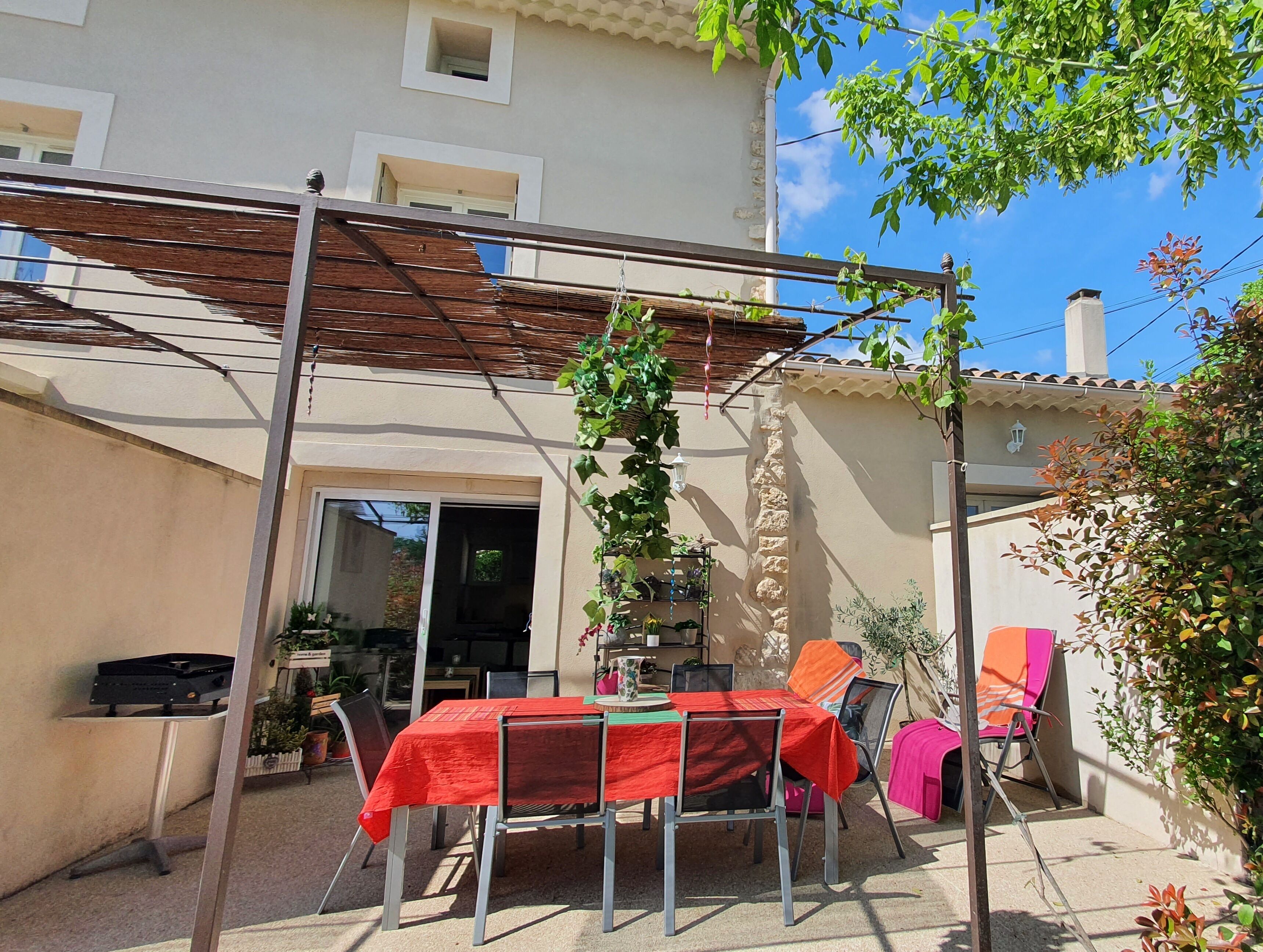 A covered patio area with a table and chairs, a pergola, and a stone wall.
