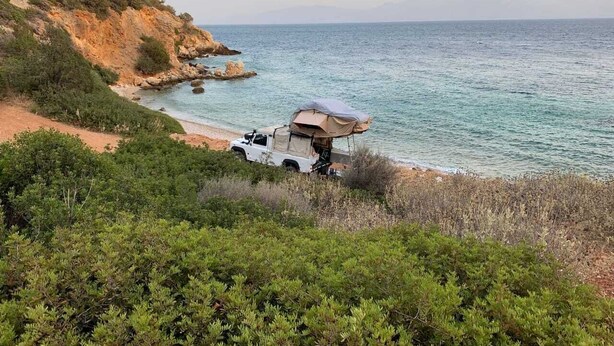 Ett fordon med ett tak monterat ovanpå är parkerat på en strand med stenig mark och vegetation.