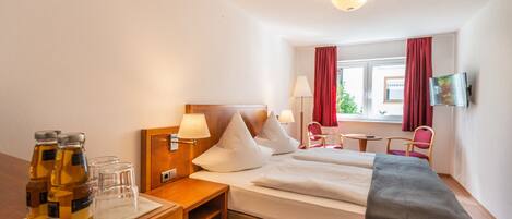 A hotel room with a bed, bedside tables, a desk, a chair, a TV, and a window with curtains.