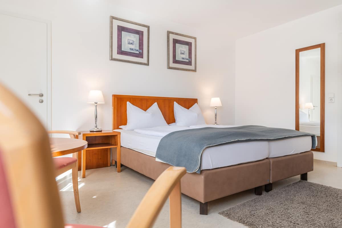 Habitación de hotel con una cama doble, dos mesitas de noche con lámparas, un cabecero de madera, un pequeño escritorio de madera y una silla.