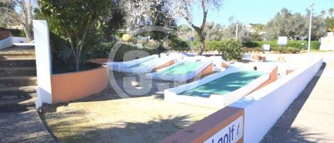 Un campo de mini golf con varias pistas, un letrero que indica la ubicación y follaje circundante.