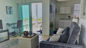 Ein Wohnzimmer mit grauem Sofa, einem Couchtisch und einem Deckenventilator. Eine Tür führt zu einem Balkon.