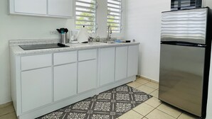 Eine Küche mit weißen Schränken, einem Edelstahlkühlschrank, einer Spüle und einem Fenster mit Jalousien.