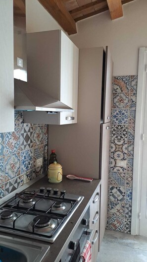 A kitchen with a gas stove, a stainless steel range hood, and a refrigerator. The walls are decorated with patterned tiles. - Villa located two kilometers from the kitesurfing schools (MARSALA)