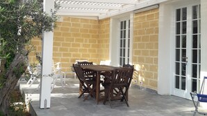 Un patio couvert avec un mur en pierre, une table en bois avec des chaises et une structure de pergola blanche.