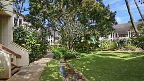 A well-maintained garden with a small stream, lush greenery, and a pathway leading to a building. - Waikomo Stream Villas 302 | Updated 1BR Condo w/ Cal King, AC, Murphy Bed (Koloa)