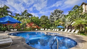 A swimming pool with lounge chairs and umbrellas, surrounded by tropical vegetation. - Waikomo Stream Villas 302 | Updated 1BR Condo w/ Cal King, AC, Murphy Bed (Koloa)